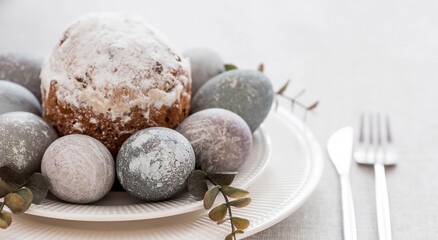 Spring table setting. A plate with a cotton napkin with a bunny, a cake and Easter eggs. Silverware, Easter bunnies and a vase of flowers on a linen tablecloth. The concept of a bright Easter holiday.