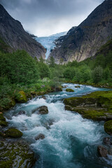 Fototapeta na wymiar Mountain river with ice cold water of Briksdalsbreen glacier in the mountains of Jostedalsbreen national park in Norway, moody atmosphere, rocks in the water