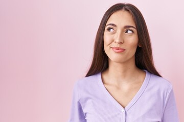 Fototapeta premium Young hispanic woman with long hair standing over pink background smiling looking to the side and staring away thinking.