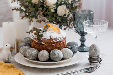 Spring table setting. A plate with a cotton napkin with a bunny, a cake and Easter eggs. Silverware, Easter bunnies and a vase of flowers on a linen tablecloth. The concept of a bright Easter holiday.