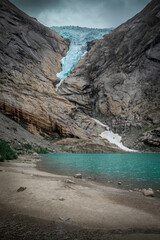 Obraz premium Briksdalsbreen glacier in the mountains of Jostedalsbreen national park in Norway, turquoise glacier lake and blue ice, rocks along the beach