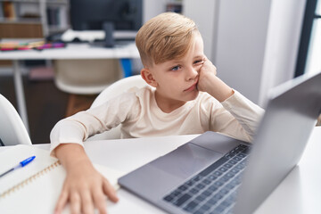 Adorable toddler student boring using laptop sitting on table at classroom