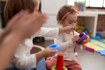 Obraz premium Adorable caucasian girl playing with hoops sitting on floor at kindergarten