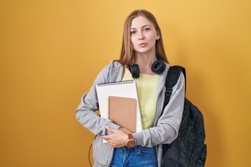 Young caucasian woman wearing student backpack and holding books looking at the camera blowing a kiss on air being lovely and sexy. love expression.