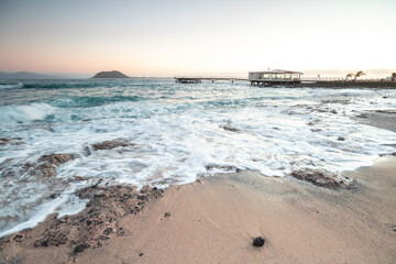 Beautiful morning on the sandy beach. Long exposure at the sea. Milky sunrise in haze and fog. Corralejo, Canary Islands, Spain