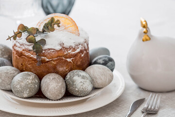 Spring table setting. A plate with a cotton napkin with a bunny, a cake and Easter eggs. Silverware, Easter bunnies and a vase of flowers on a linen tablecloth. The concept of a bright Easter holiday.