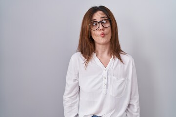Fototapeta premium Brunette woman standing over white isolated background making fish face with lips, crazy and comical gesture. funny expression.