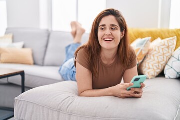 Young woman using smartphone lying on sofa at home