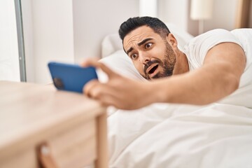 Young hispanic man waking up for alarm smartphone at bedroom