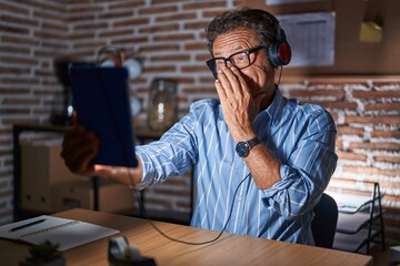 Middle age hispanic man using touchpad sitting on the table at night laughing and embarrassed...