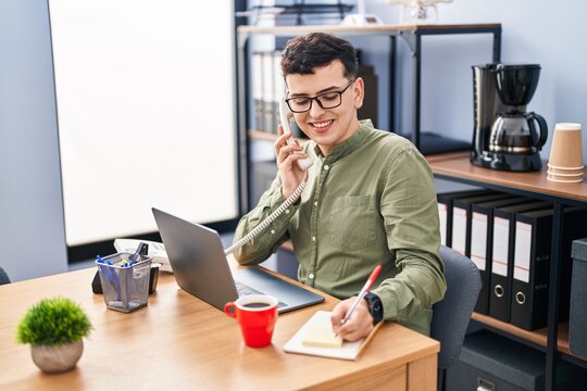 Young non binary man business worker using laptop talking on telephone at office