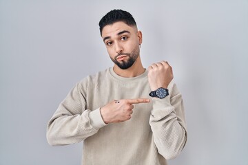 Young handsome man standing over isolated background in hurry pointing to watch time, impatience,...