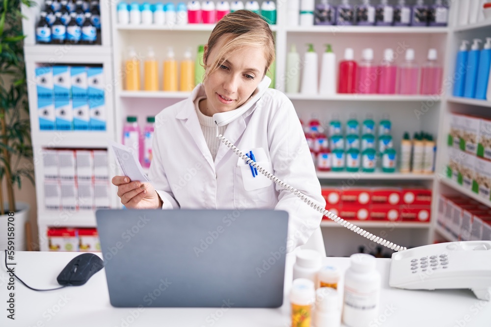 Poster young blonde woman pharmacist talking on telephone using laptop at pharmacy