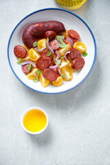 Plate of warm chorizo and yellow tomato salad, flat lay on a light-grey granite background, vertical shot with copy space