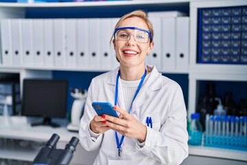 Young blonde woman scientist smiling confident using smartphone at laboratory