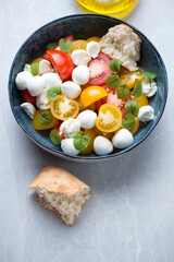 Bowl of tomato salad with mini mozzarella balls and fresh beetroot leaves on a light-grey granite background, vertical shot