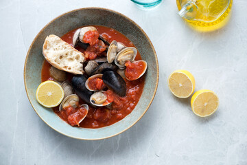 Plate of tomato broth with mussels and vongole on a light-grey granite background, horizontal shot, view from above