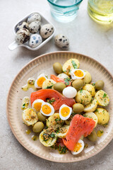 Salad with baby potato, red fish fillet, quail eggs and green olives, vertical shot on a beige stone background