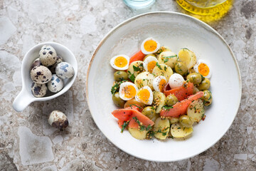 Plate with potato, smoked trout fillet and quail eggs salad, above view on a light-brown granite background, horizontal shot