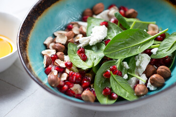 Closeup of salad with fresh spinach leaves, pomegranate seeds, goat cheese and hazelnuts, selective focus