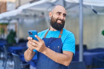 Young bald man waiter smiling confident using smartphone at coffee shop terrace