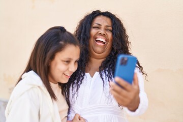 Mother and daughter hugging each other watching video on smartphone at street