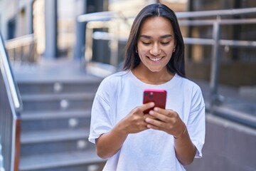 Young beautiful hispanic woman smiling confident using smartphone at street