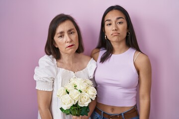 Hispanic mother and daughter holding bouquet of white flowers looking sleepy and tired, exhausted for fatigue and hangover, lazy eyes in the morning.
