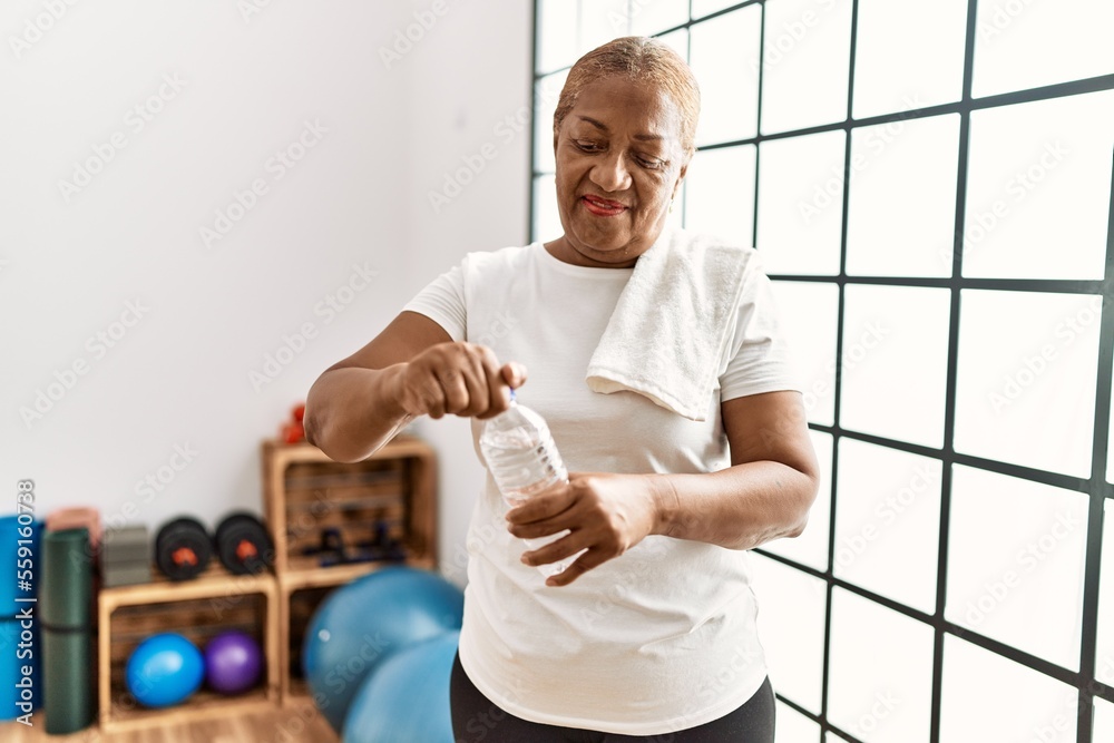 Wall mural Senior african american woman smiling confident drinking water at sport center