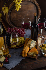 Cheese and wine tasting still life. Glass of wine, bottle of wine, grape in front of the rustic wooden barrels for beverage in a dark wine cellar. Nuts, honey, dipper. Empty copy space, mock up