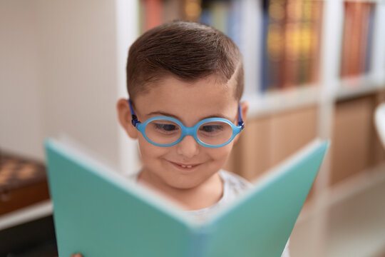 Adorable hispanic toddler student smiling confident reading book at library school