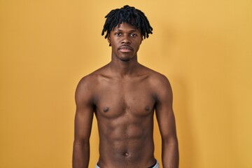 Fototapeta premium Young african man with dreadlocks standing shirtless relaxed with serious expression on face. simple and natural looking at the camera.
