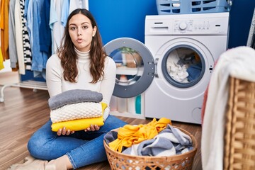 Young hispanic woman holding clean laundry making fish face with mouth and squinting eyes, crazy and comical.