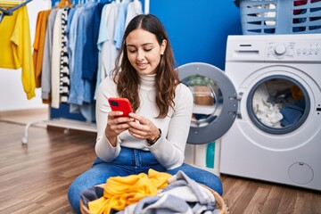 Young beautiful hispanic woman smiling confident using smartphone at laundry room