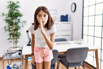 Young hispanic girl standing at pediatrician clinic hand on mouth telling secret rumor, whispering malicious talk conversation