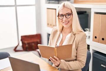 Young blonde woman business worker writing on notebook working at office