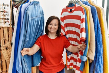 Brunette woman with down syndrome standing between hangers with different clothes at retail shop