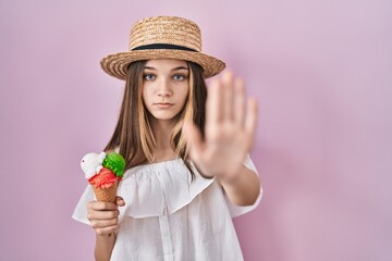 Teenager girl holding ice cream doing stop sing with palm of the hand. warning expression with negative and serious gesture on the face.