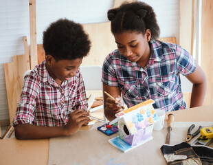 Two African American brothers and sisters help each other make wooden signs to celebrate the Christmas season in the workshop..