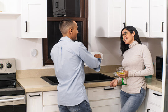 A young man doing housework in the kitchen while talking with his wife.
