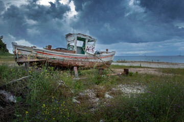 Fototapeta na wymiar Abandoned old fishing boat ashore. Coast of Corfu Greece. Clouds. Sea. Shipwreck.