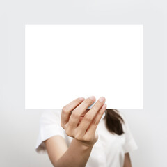 Young woman holding blank white paper at face on gray background. advertising copy space.