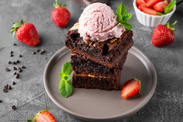 Chocolate brownie pieces with nuts, strawberry and ice cream on a plate on a dark background. Selective focus.