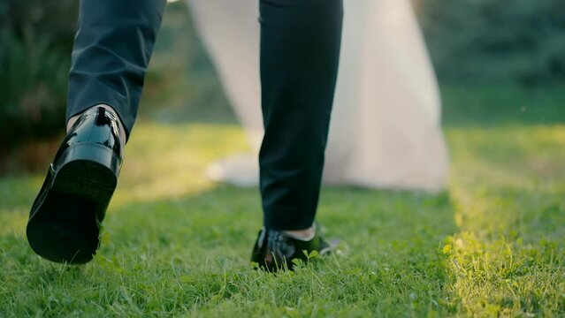 Close up slow motion shot of legs of groom approaching bride standing on green grass in park at day.