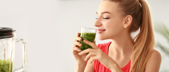 Fototapeta premium Pretty young woman drinking green smoothie at home