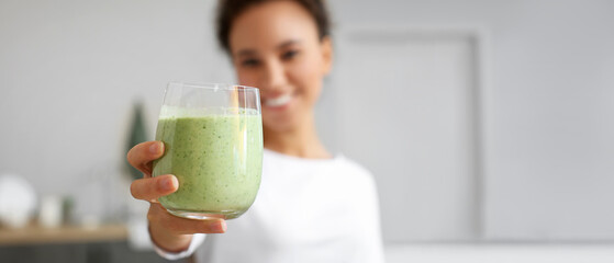 Young African-American woman with fresh green smoothie in kitchen, closeup