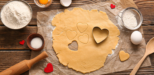 Fototapeta na wymiar Raw dough and ingredients for preparing tasty heart shaped cookies on wooden background. Valentines Day celebration