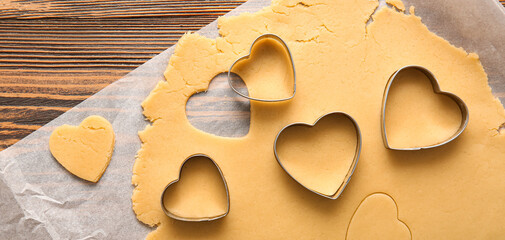 Dough for preparing tasty cookies and heart shaped cutters on wooden background. Valentines Day...