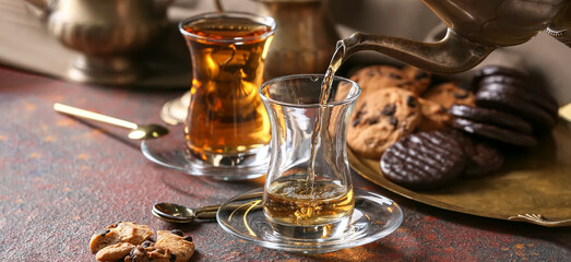Pouring of hot Turkish tea in glass cup on table