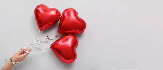 Female hand with red heart-shaped balloons on light background. Banner for Valentine's Day